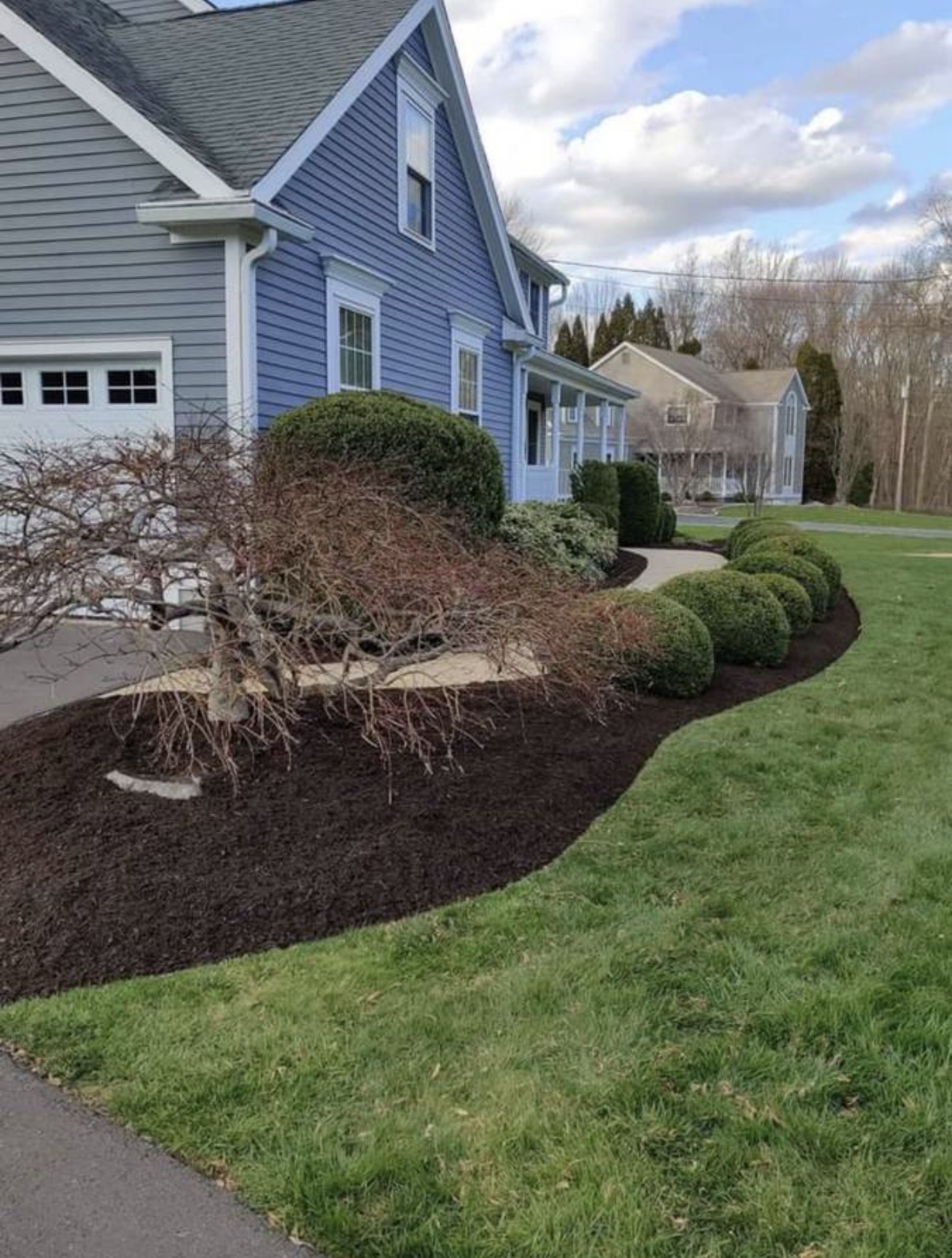 Finished curved front garden bed with dark mulch beside a blue house