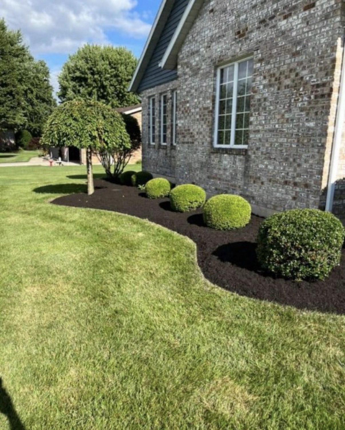 Finished foundation bed with fresh dark mulch and a curved edge beside the brick home